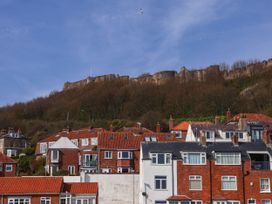 A row of houses with red roofs in front of a wooded hill and old stone castle walls at Apartment 3 in Scarborough