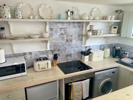 A kitchen with appliances and dishes on shelves at The Cow Shed in Mawgan Porth