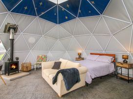 A dome-shaped room with a bed, sofa, wood burning stove, and a small chair at Meadow View - Bryn-Mawr Retreat in Brynmawr near Llanymynech