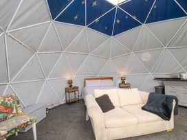 An interior of a dome with a bed two bedside tables with lamps a beige sofa with cushions a floral chair and a kitchenette at Meadow View - Bryn-Mawr Retreat in Brynmawr near Llanymynech