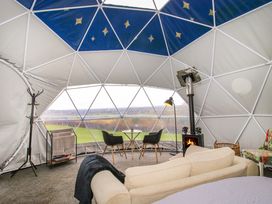 Interior of a dome tent with a beige sofa a small round table with two chairs a wood stove and a view of the countryside at Meadow View - Bryn-Mawr Retreat in Brynmawr near Llanymynech