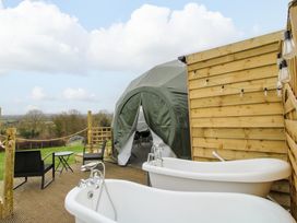An outdoor deck with two white bathtubs black chairs and a green tent structure at Meadow View - Bryn-Mawr Retreat in Brynmawr near Llanymynech