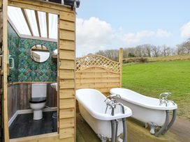 An outdoor bathroom with two white clawfoot bathtubs and a wooden structure housing a toilet and sink at Meadow View - Bryn-Mawr Retreat in Brynmawr near Llanymynech
