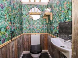 A bathroom with a toilet sink floral patterned wallpaper wooden paneling a round mirror and a small shelf at Meadow View - Bryn-Mawr Retreat Brynmawr near Llanymynech