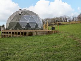 A geodesic dome on a wooden raised platform in a grassy field with trees in the background at Meadow View - Bryn-Mawr Retreat in Brynmawr near Llanymynech