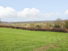 A grassy field with hedges and trees overlooking distant farmland under a partly cloudy sky at Meadow View - Bryn-Mawr Retreat in Brynmawr near Llanymynech
