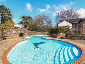 An outdoor swimming pool with steps and a dolphin design by a stone wall and buildings at Millers Loft in Modbury