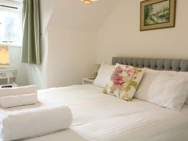 A bedroom with a bed with white linens and floral pillow near a window with green curtains at Millers Loft in Modbury