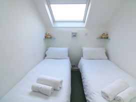 A small bedroom with two single beds under a skylight each bed has white linens rolled towels and a stuffed animal on a shelf at Millers Loft in Modbury