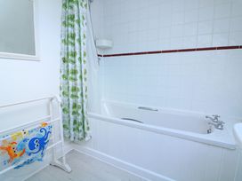 A bathroom with a white bathtub a shower curtain with green leaves and a towel rack with a colorful towel at Millers Loft in Modbury