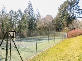 An outdoor tennis court surrounded by a chain link fence with trees and bushes around at Millers Loft in Modbury