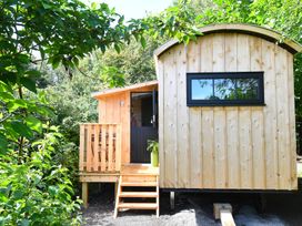 Small wooden cabin with steps and a porch surrounded by green trees at Bugail Hut in Llantwit Major