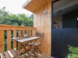 An outdoor wooden deck with a small table and two chairs with drinks on the table at Bugail Hut in Llantwit Major