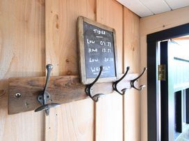 A wooden wall with a coat rack with four metal hooks and a chalkboard with tide times at Bugail Hut in Llantwit Major