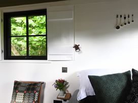 A bedroom corner with a bed and pillows a window with leafy green trees outside and a small vase with flowers on a wooden chair at Bugail Hut in Llantwit Major