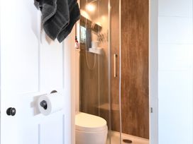 A bathroom door with towels and toilet paper holder next to a shower with glass door and brown wall panels at Bugail Hut in Llantwit Major