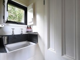 A utility room with a white sink black countertop a window and two bottles at Bugail Hut in Llantwit Major