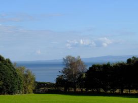A grassy field with trees and a gate overlooking a body of water and distant hills at Bugail Hut in Llantwit Major