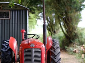 A red tractor parked near a corrugated metal shed with trees in the background at Bugail Hut in Llantwit Major