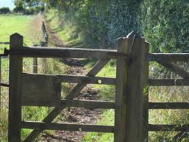 A wooden gate on a dirt path with green fields and trees at Bugail Hut in Llantwit Major