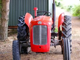 A red tractor with large rear tires parked on a dirt path near a tree and a corrugated metal structure at Bugail Hut in Llantwit Major