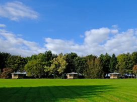 A grassy field with three wooden shelters in front of trees at Bugail Hut in Llantwit Major