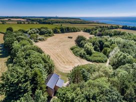 A field surrounded by trees with a small building and an ocean in the background at Bugail Hut in Llantwit Major