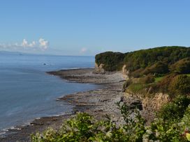 A rocky coastline with cliffs and trees overlooking the sea at Bugail Hut in Llantwit Major