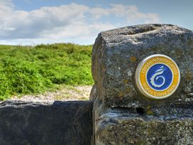 A stone marker with a Wales Coast Path emblem on a grassy landscape at Bugail Hut in Llantwit Major