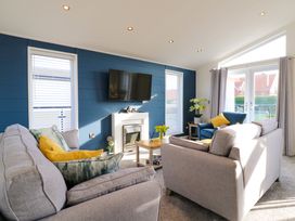A living room with sofas a TV on a blue wall and sliding doors at Number 43 The Poplars in Burnham Market