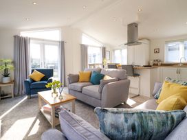 A living room with sofas a chair a coffee table flowers and an open kitchen at Number 43 The Poplars in Burnham Market