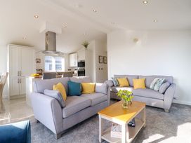 A living room with two gray sofas and a wooden coffee table with flowers next to an open kitchen at Number 43 The Poplars in Burnham Market