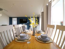 A dining table set with bowls and glasses next to chairs in a room with a television on a blue wall at Number 43 The Poplars Burnham Market
