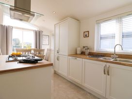 A kitchen with white cabinets a gas stove and a dining area with chairs at Number 43 The Poplars in Burnham Market