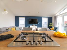 A kitchen island with a gas stove and bowls of lemons overlooking a living room with sofas chairs and a wall mounted tv at Number 43 The Poplars in Burnham Market