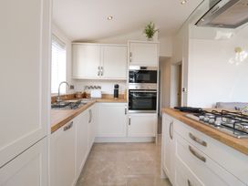 A kitchen with white cabinets wooden countertops a built in oven a gas stove and a sink at Number 43 The Poplars in Burnham Market