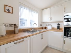 A kitchen with white cabinets wooden countertops a sink with drying rack a toaster a knife block and appliances at Number 43 The Poplars in Burnham Market