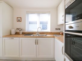 A kitchen with white cabinets a wooden countertop a sink a dish rack a kettle and built in ovens at Number 43 The Poplars in Burnham Market