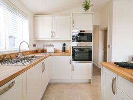 A kitchen with white cabinets a wooden countertop a sink with a drying rack built in oven and microwave at Number 43 The Poplars in Burnham Market