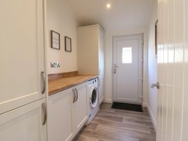 A utility room with white cabinets a washing machine wooden countertop and a door at Number 43 The Poplars in Burnham Market