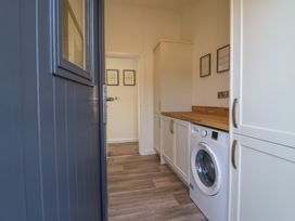 A laundry room with a washing machine wooden countertop white cabinets and wall art at Number 43 The Poplars Burnham Market