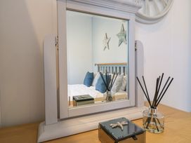 A wooden table with a mirror reflecting a bed with pillows and star wall decorations at Number 43 The Poplars in Burnham Market