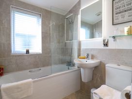 A bathroom with bathtub shower white sink toilet and a window with blinds at Number 43 The Poplars in Burnham Market