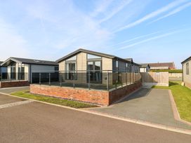 A modern single-story house with a raised patio and glass railing on a paved driveway at Number 43 The Poplars in Burnham Market