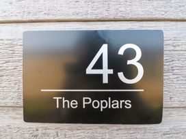 A black house number sign with white text showing number 43 and The Poplars on a wooden wall at Number 43 The Poplars in Burnham Market