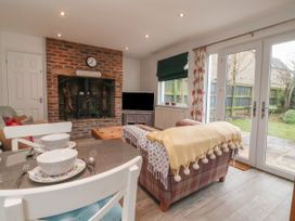 A living room with a brick fireplace a TV and glass doors leading to a garden at Ellesmere Cottage in Hornsea