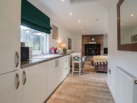 A kitchen area with white cabinets and a sink leading to a living room with a brick fireplace at Ellesmere Cottage in Hornsea