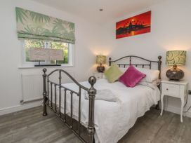 A bedroom with a metal bed frame two bedside tables with lamps and a window with patterned curtains at Ellesmere Cottage in Hornsea