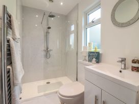 A bathroom with a shower, toilet, sink, heated towel rack with towels, and a window at Ellesmere Cottage in Hornsea