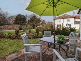 A garden patio with table chairs and a green umbrella overlooking a white house at Ellesmere Cottage in Hornsea